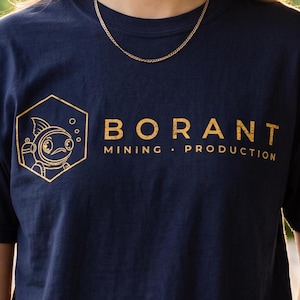 May include: A navy blue short-sleeve t-shirt featuring a gold-colored graphic of a fish in a diving helmet inside a hexagon. To the right of the graphic, the text reads BORANT MINING PRODUCTION in a distressed, gold-colored font.