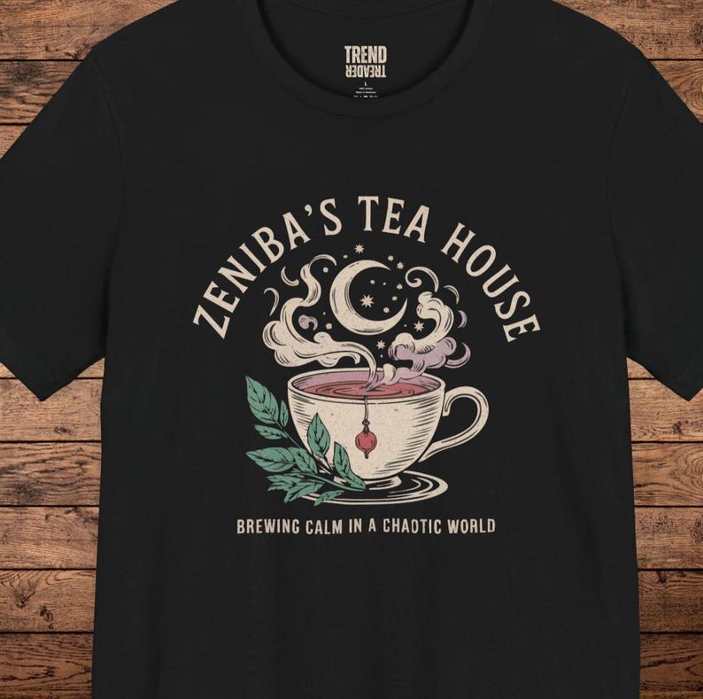 May include: Black t-shirt with a white graphic design of a teacup with steam and a crescent moon. The text "Zeniba's Tea House" is written in a circular pattern around the teacup. The text "Brewing Calm in a Chaotic World" is written below the graphic.