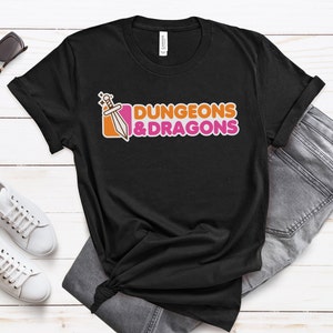 Könnte beinhalten: Schwarzes T-Shirt mit einem pinkfarbenen und orangenen Logo, auf dem "Dungeons & Dragons" steht. Das Logo zeigt ein Schwert mit einem Stern oben drauf.