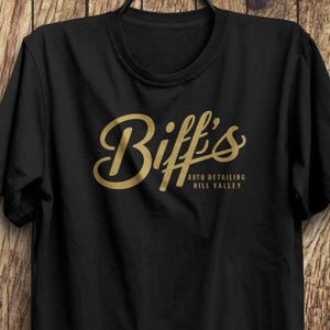 May include: Black t-shirt with a gold graphic of the text "Biff's Auto Detailing Hill Valley".