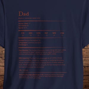 May include: Navy blue t-shirt with the word "Dad" at the top, followed by game stats. The text includes "Armor Class 17", "Hit Points 68", and "Speed 30 ft.". The shirt also lists skills and actions.