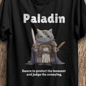 May include: A black t-shirt with a white graphic of a cat wearing armor and holding a sword. The text "Paladin" is above the cat and the text "Sworn to protect the innocent and judge the annoying." is below the cat.