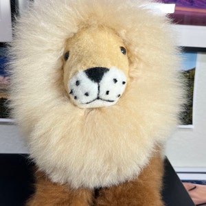 Op de afbeelding: Een pluche leeuwenknuffel met een lichtbruine manen en een bruin gezicht. De leeuw heeft zwarte ogen, een zwarte neus en witte snorharen.