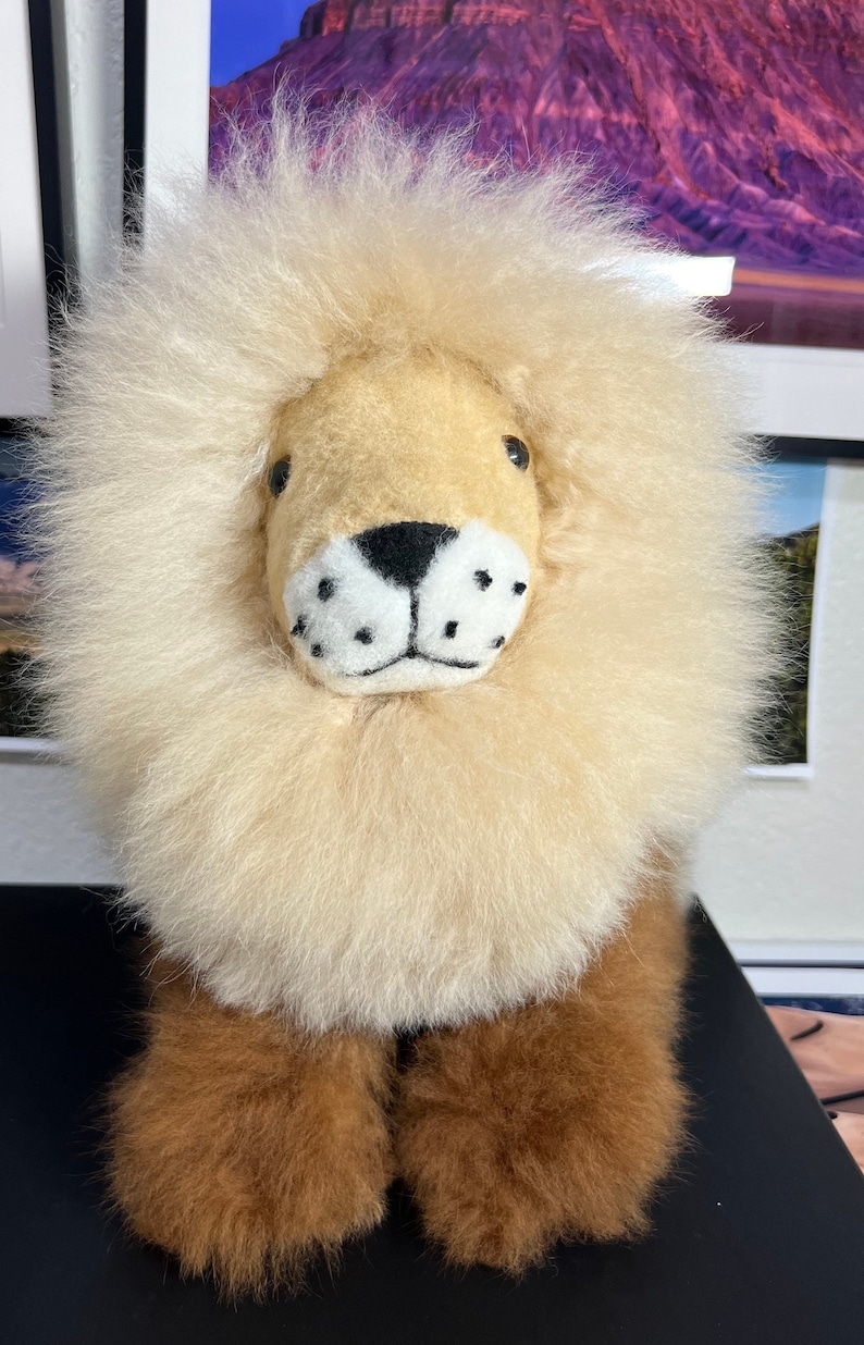Op de afbeelding: Een pluche leeuwenknuffel met een lichtbruine manen en een bruin gezicht. De leeuw heeft zwarte ogen, een zwarte neus en witte snorharen.