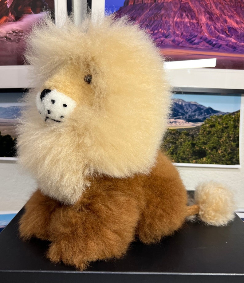Op de afbeelding: Een pluche leeuwenknuffel met een lichtbruin lichaam en een pluche, cr&egrave;mekleurige manen. De leeuw heeft een zwarte neus en zwarte ogen.
