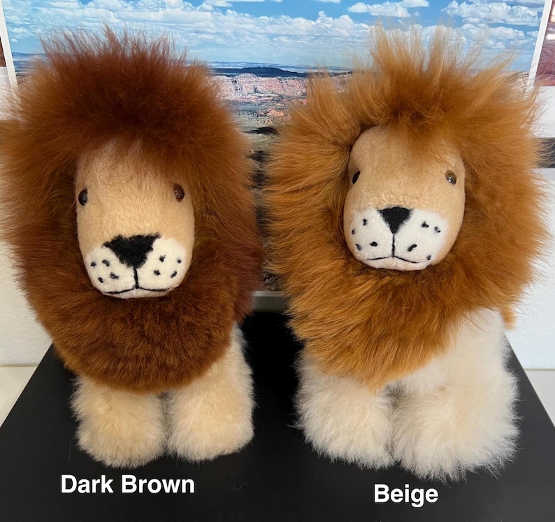 Op de afbeelding: Twee pluche leeuwen speelgoed, een met donkerbruine vacht en de andere met beige vacht. Beide hebben een wit gezicht met zwarte ogen en een zwarte neus.