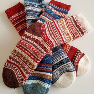 May include: Five pairs of colorful patterned socks with white toes and heels. The socks feature a variety of geometric and striped designs in shades of red, blue, brown, and white.