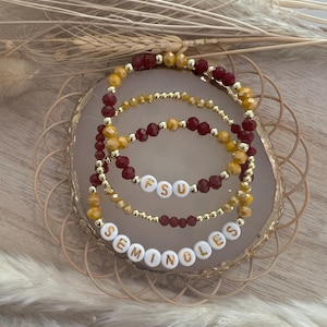 May include: Three beaded bracelets with gold and maroon beads. The bracelets spell out "FSU Seminoles" in gold letters on white beads.