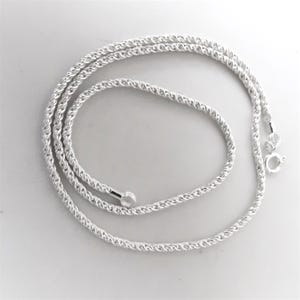 May include: A silver-coloured rope chain necklace. The chain is made of tightly woven strands, creating a textured appearance. The necklace has a clasp closure and a small loop at the other end.
