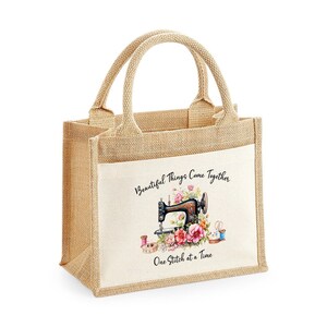 May include: A beige burlap tote bag with a white fabric panel featuring a vintage sewing machine with pink flowers and the text "Beautiful Things Come Together One Stitch at a Time".