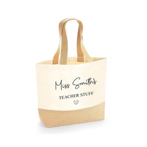 K&ouml;nnte beinhalten: Beige Canvas-Tragetasche mit Juteboden und passenden Griffen. Auf der Tasche steht in schwarzer Schrift "Miss Smith's TEACHER STUFF" mit einem kleinen Herzsymbol darunter, ideal f&uuml;r Lehrer.