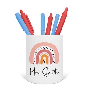 May include: White ceramic pencil holder with a rainbow design and black polka dots. The rainbow is in shades of pink, orange, and yellow. The text "Mrs. Smith" is written below the rainbow.
