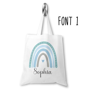 K&ouml;nnte beinhalten: Wei&szlig;e Einkaufstasche mit einem blauen und gr&uuml;nen Regenbogen-Design und dem Namen "Sophia" darunter gedruckt.
