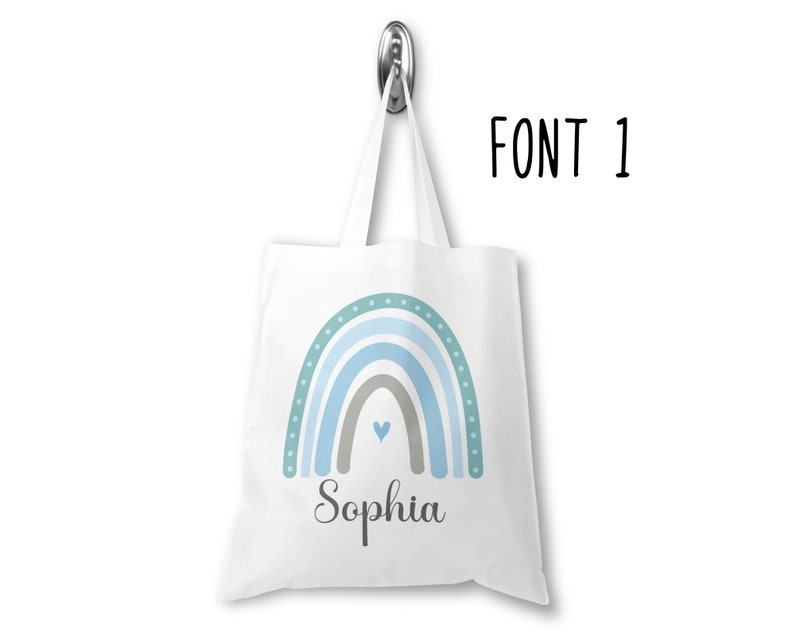 K&ouml;nnte beinhalten: Wei&szlig;e Einkaufstasche mit einem blauen und gr&uuml;nen Regenbogen-Design und dem Namen "Sophia" darunter gedruckt.