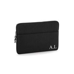 May include: Black laptop sleeve with a zipper closure and a small pocket. The initials "A.L" are printed in white on the lower right corner. The sleeve is made of a textured material.
