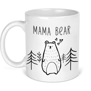 May include: White ceramic mug with a black outline of a mama bear and the text "MAMA BEAR" printed on the front. The bear is surrounded by small trees and hearts.