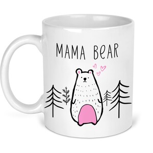 May include: White ceramic mug with a black outline of a bear and the text "MAMA BEAR" in black. The bear has pink accents and is surrounded by small pink hearts.