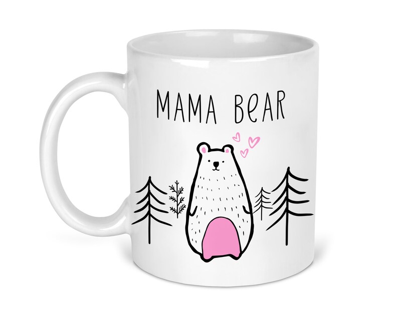 May include: White ceramic mug with a black outline of a bear and the text "MAMA BEAR" in black. The bear has pink accents and is surrounded by small pink hearts.
