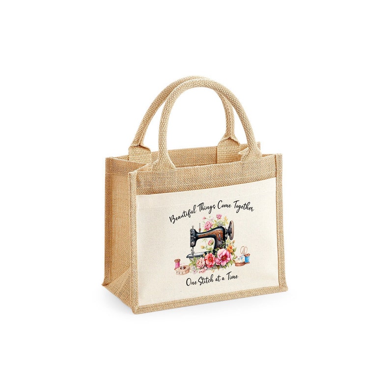 May include: A beige burlap tote bag with a white fabric panel featuring a vintage sewing machine with pink flowers and the text "Beautiful Things Come Together One Stitch at a Time".