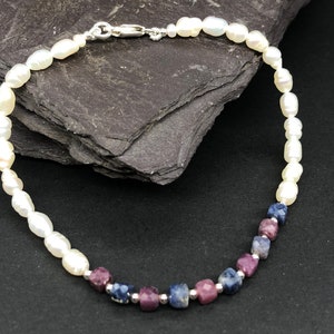 May include: A white pearl bracelet with a silver clasp and a row of purple and blue gemstone beads.