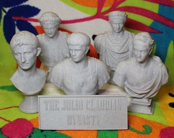 May include: Five gray plaster busts of Roman emperors, including Julius Caesar, Augustus, Tiberius, Caligula, and Claudius, arranged on a colorful beach towel with a sign that reads "The Julio Claudian Dynasty".