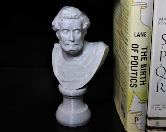 May include: A white marble bust of a man with a beard, on a white marble base. The bust is sitting on a shelf next to two books. The book on the left has the title "The Birth of Politics" by Lane. The book on the right has the title "SPQR" by Mary Beard.