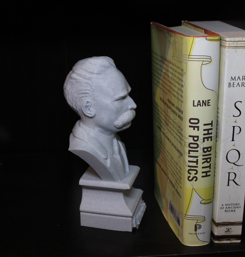 Puede incluir: Un busto de escultura blanca de un hombre con bigote, sobre un pedestal blanco. El busto est&aacute; colocado en una estanter&iacute;a junto a dos libros. El libro de la izquierda tiene el t&iacute;tulo "The Birth of Politics" de Lane, y el libro de la derecha tiene el t&iacute;tulo "SPQR" de Mary Beard.