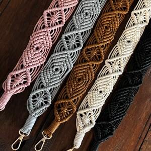 May include: Five macrame straps in different colors, including pink, gray, brown, white, and black. Each strap has a gold metal clasp.