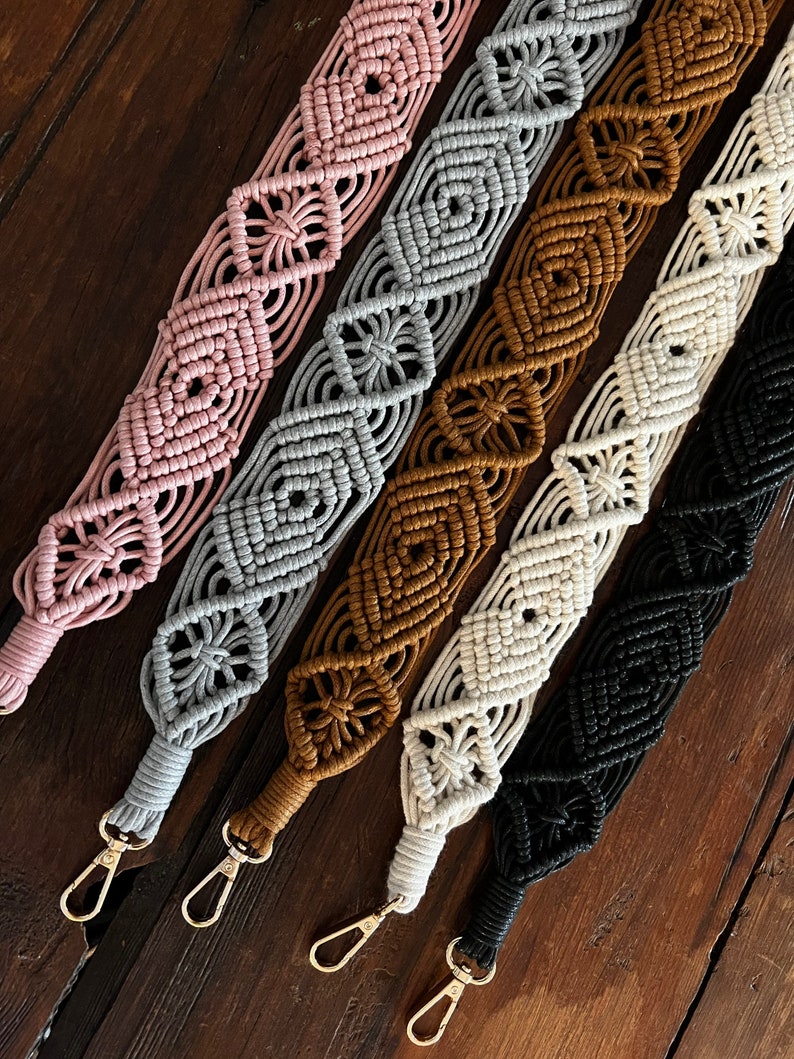 May include: Five macrame straps in different colors, including pink, gray, brown, white, and black. Each strap has a gold metal clasp.