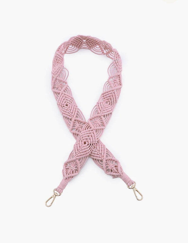 May include: A pink macrame bag strap with gold metal clasps. The strap is made of a thick, woven cord and has a geometric pattern.