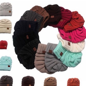 May include: A collection of 18 knitted beanies in various colors, including gray, black, brown, beige, red, pink, and blue. The beanies have a slouchy, relaxed fit and feature a small leather patch on the side.