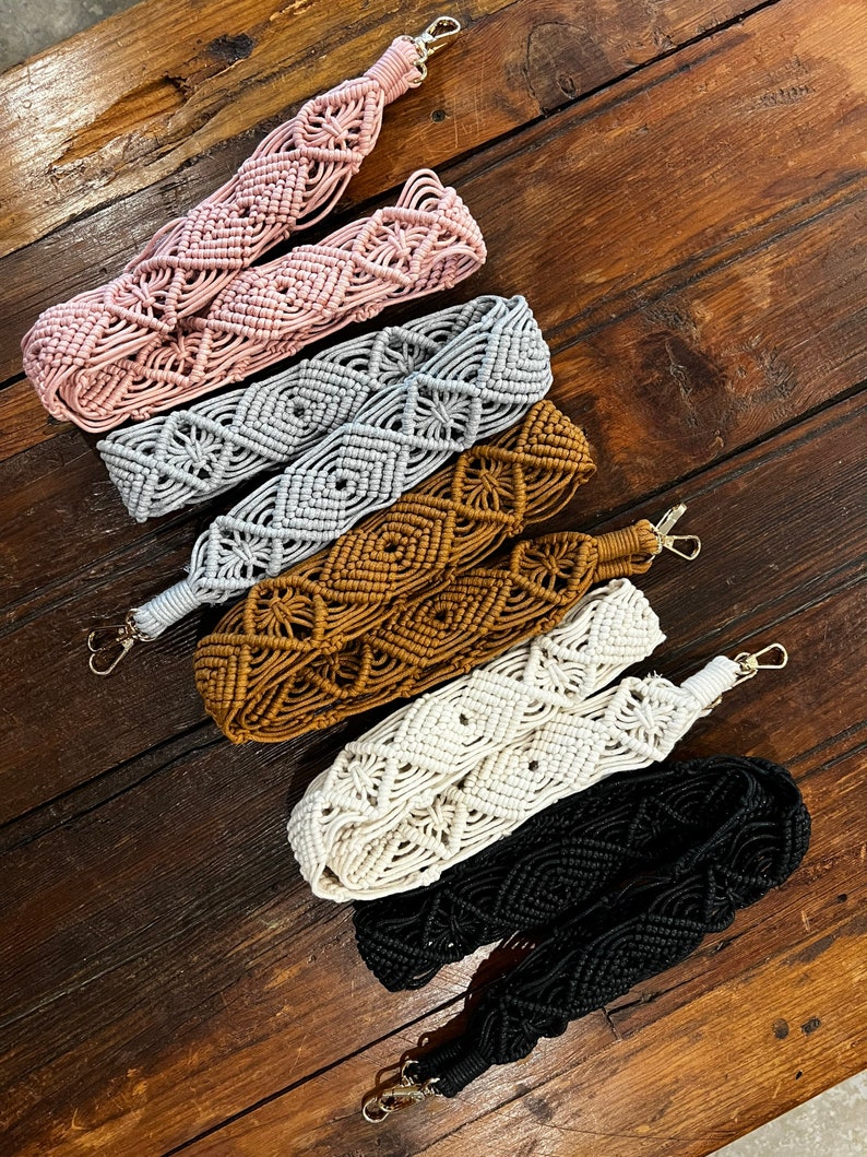May include: Five macrame bag straps in different colors: pink, gray, brown, white, and black. The straps are made of woven cord and have a diamond pattern.