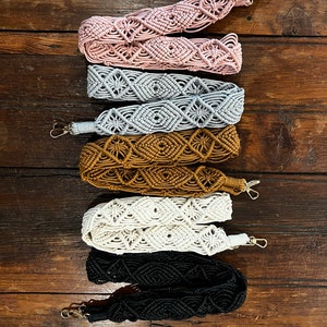 May include: Five different colored macrame straps with metal clasps. The straps are pink, gray, brown, white, and black.