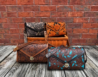 May include: Four leather purses with floral tooled designs. The purses are brown, tan, and blue with black accents. The purses are arranged in a pyramid shape on a wooden surface.