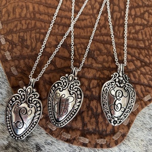 May include: Three silver necklaces with heart-shaped pendants. Each pendant features a different initial, S, L, and E, engraved in a decorative script.