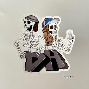 May include: A sticker featuring two cartoon skeletons. One skeleton wears a gray beanie and has red hair, while the other wears a blue baseball cap and has long brown hair. They are holding a gray block with the letters "DH" on it. The word "CLEAR" is at the bottom.