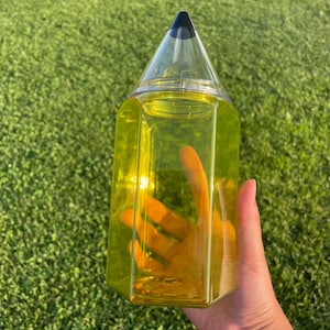 May include: A yellow pencil-shaped water bottle with a black top. The bottle is clear and filled with liquid.