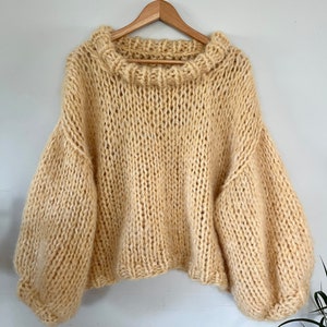 May include: A pale yellow knitted sweater with a wide, round neckline and long, puffy sleeves.