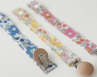 Könnte beinhalten: Drei Stoff-Schnullerketten mit Blumenmustern. Die Ketten sind an Holzperlen befestigt und haben Metallverschlüsse.