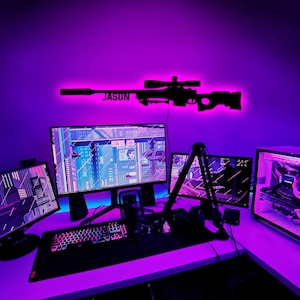 Puede incluir: Una configuración de juego púrpura y negra con un monitor de computadora, un teclado, un ratón, un micrófono y una silla de juego. El monitor de computadora muestra un videojuego. El teclado está iluminado con colores arcoíris. El ratón es negro y tiene una luz roja en la parte inferior. El micrófono es negro y tiene un soporte plateado. La silla de juego es negra y tiene un diseño púrpura y negro.