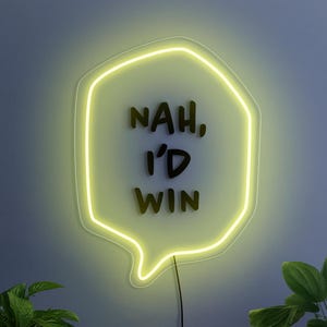 May include: A neon sign shaped like a speech bubble, with the text "NAH, I'D WIN" in black. The sign emits a bright yellow light and is mounted on a blue wall. Green plants are visible at the bottom.