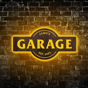 Può includere: Un cartello in legno con un bagliore giallo, che recita "Jame's Garage Est. 2023". Il cartello è su uno sfondo di muro di mattoni.