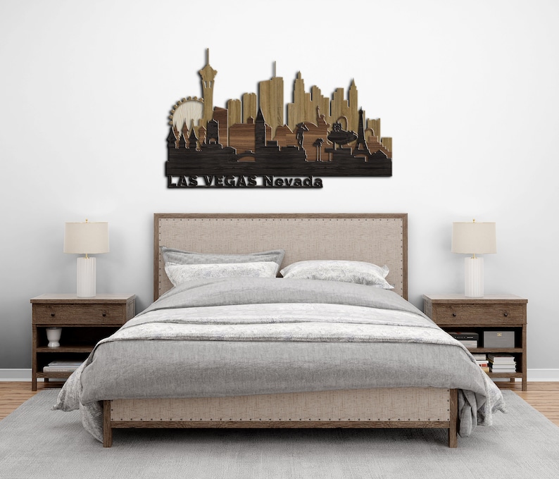 May include: A wooden wall art piece depicting the Las Vegas skyline with the text "LAS VEGAS Nevada" at the bottom. The art piece is displayed above a bed with a grey linen headboard and a grey duvet cover.