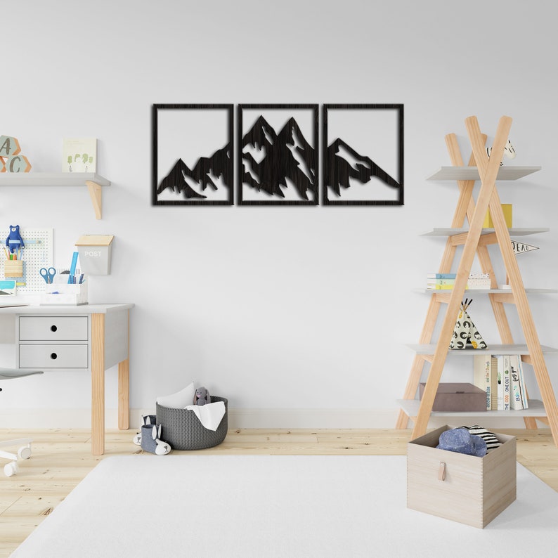 Pu&ograve; includere: Tre pezzi di arredamento da parete in legno nero con la silhouette di una catena montuosa. I pezzi sono disposti orizzontalmente e sono montati su una parete bianca.