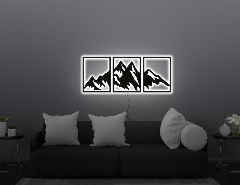 Pu&ograve; includere: Tre pezzi di arte da parete in metallo nero con un design a silhouette di montagna. I pezzi sono illuminati da dietro con luce bianca.
