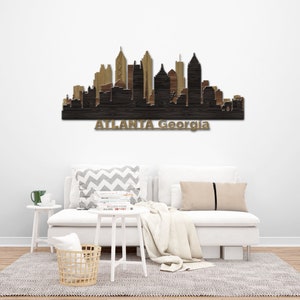 May include: Wooden wall art of the Atlanta, Georgia skyline. The artwork shows a silhouette of the city's buildings in shades of brown and black. The city name is displayed in gold lettering below the skyline.