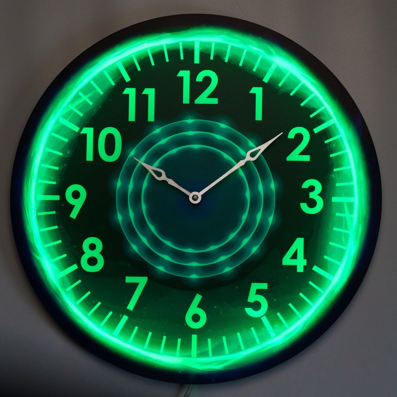 May include: A round, black clock with a green neon glow around the numbers. The clock face has a circular design in the center with concentric circles. The clock hands are silver.