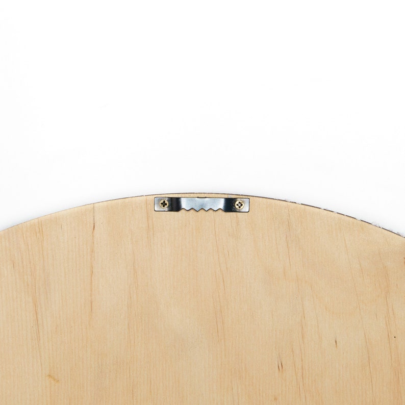 May include: The back of a round wooden frame with a metal hanging hook attached. The frame is light brown and has a smooth surface.