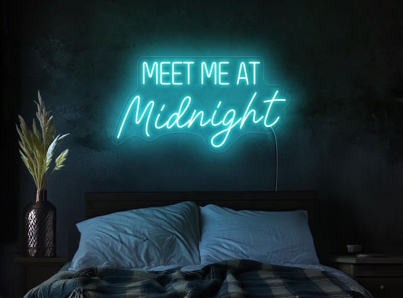 May include: A teal blue neon sign with the text "Meet Me At Midnight" on a black wall above a bed with blue and white bedding.