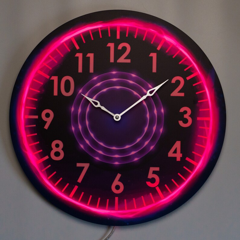 May include: A black clock with a pink neon ring around the edge. The clock face has a purple and pink swirling design in the center. The numbers are in white and the hands are silver.